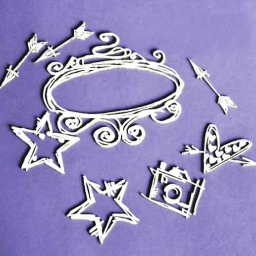 Set med utskurna kartongdekorationer, bland annat ram och pil, presenterade på bakgrund.